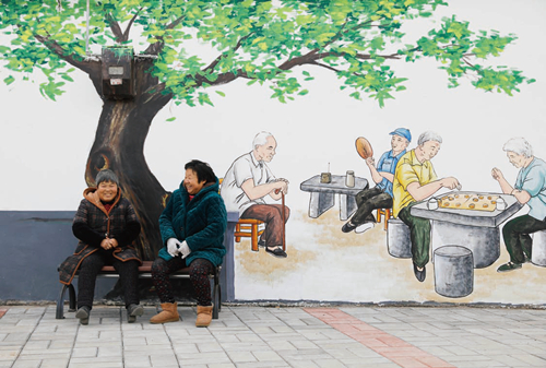 两位村民在河南省平顶山市宝丰县张八桥镇姚店铺村一处墙体画前聊天